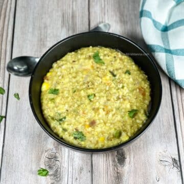 A bowl of instant pot oats khichdi is on the table and topped with cilantro.