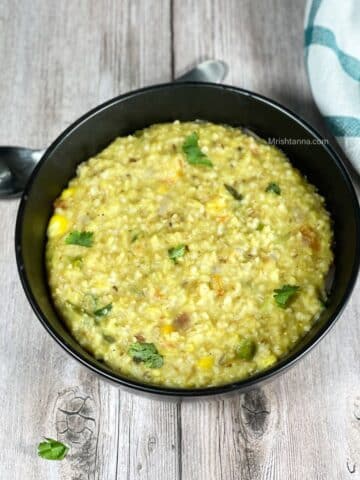 A bowl of instant pot oats khichdi is on the table and topped with cilantro.