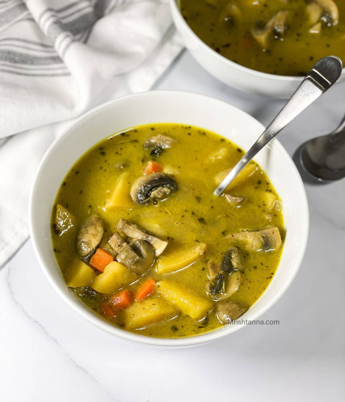 A bowl of mushroom potato soup is on the table with a spoon inserted.