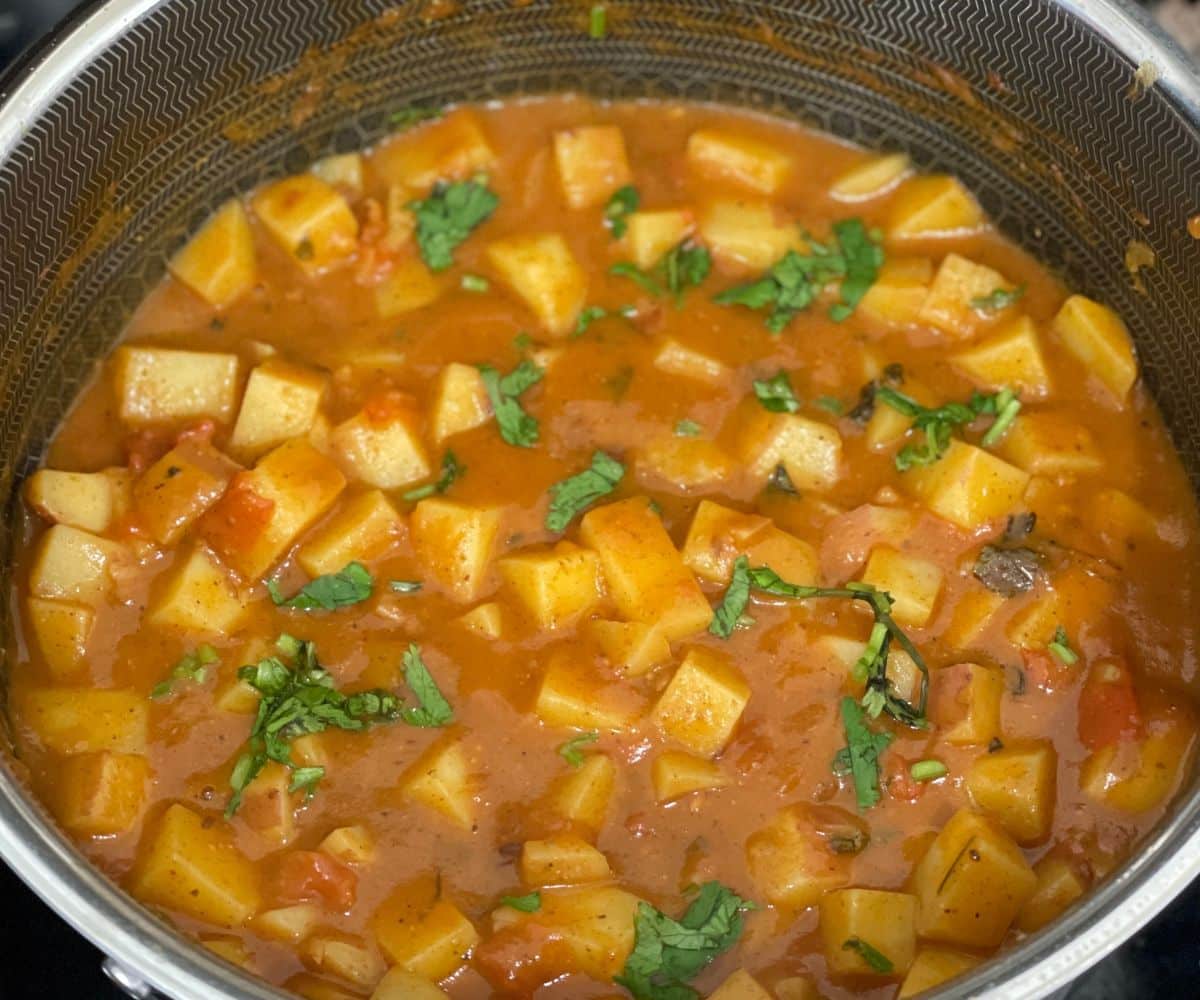 A pot of potato tomato curry is on the stove top.