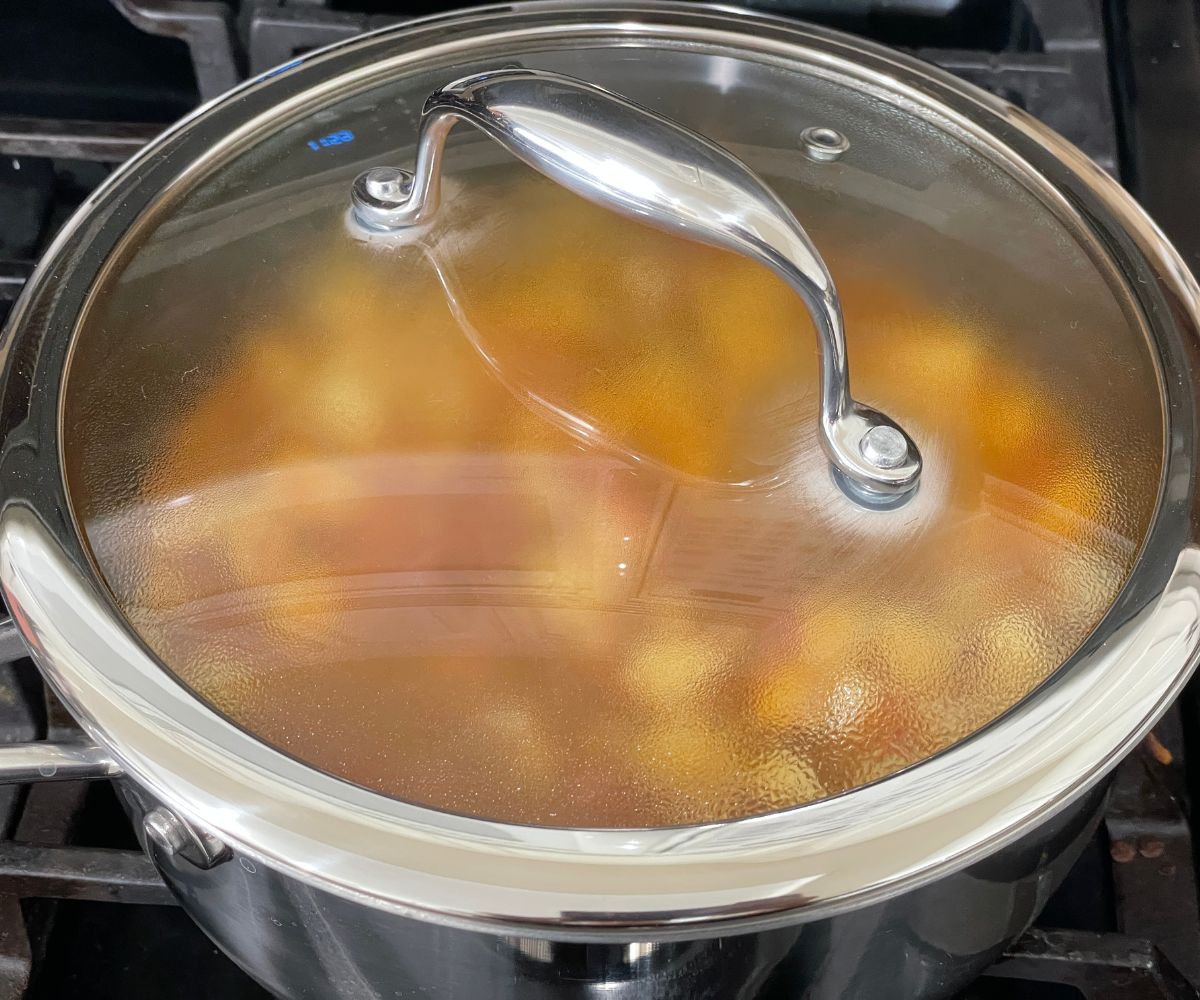 A covered pot is with potato curry over the stove top.