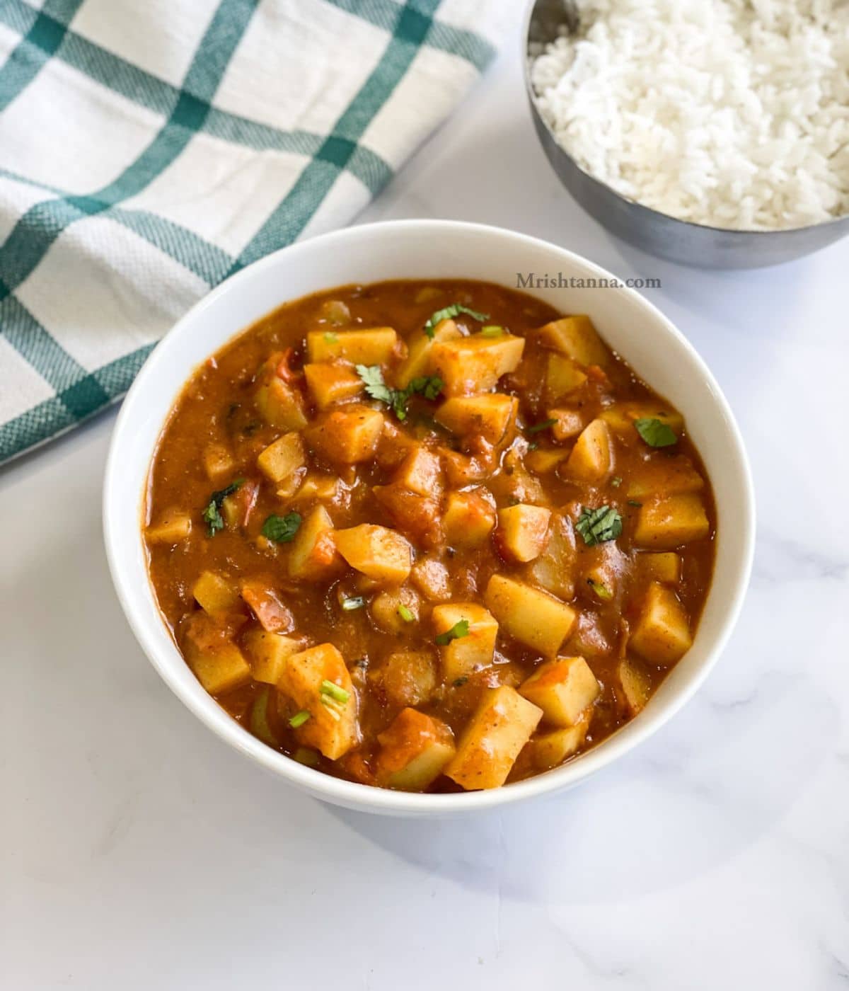 A bowl of aloo curry is on the table along with rice.