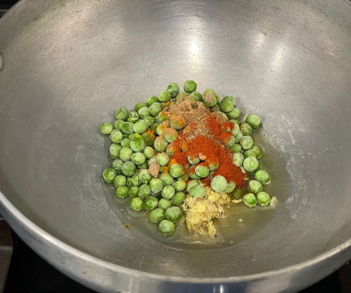 A pan is with oils, spices, and green peas over the heat.