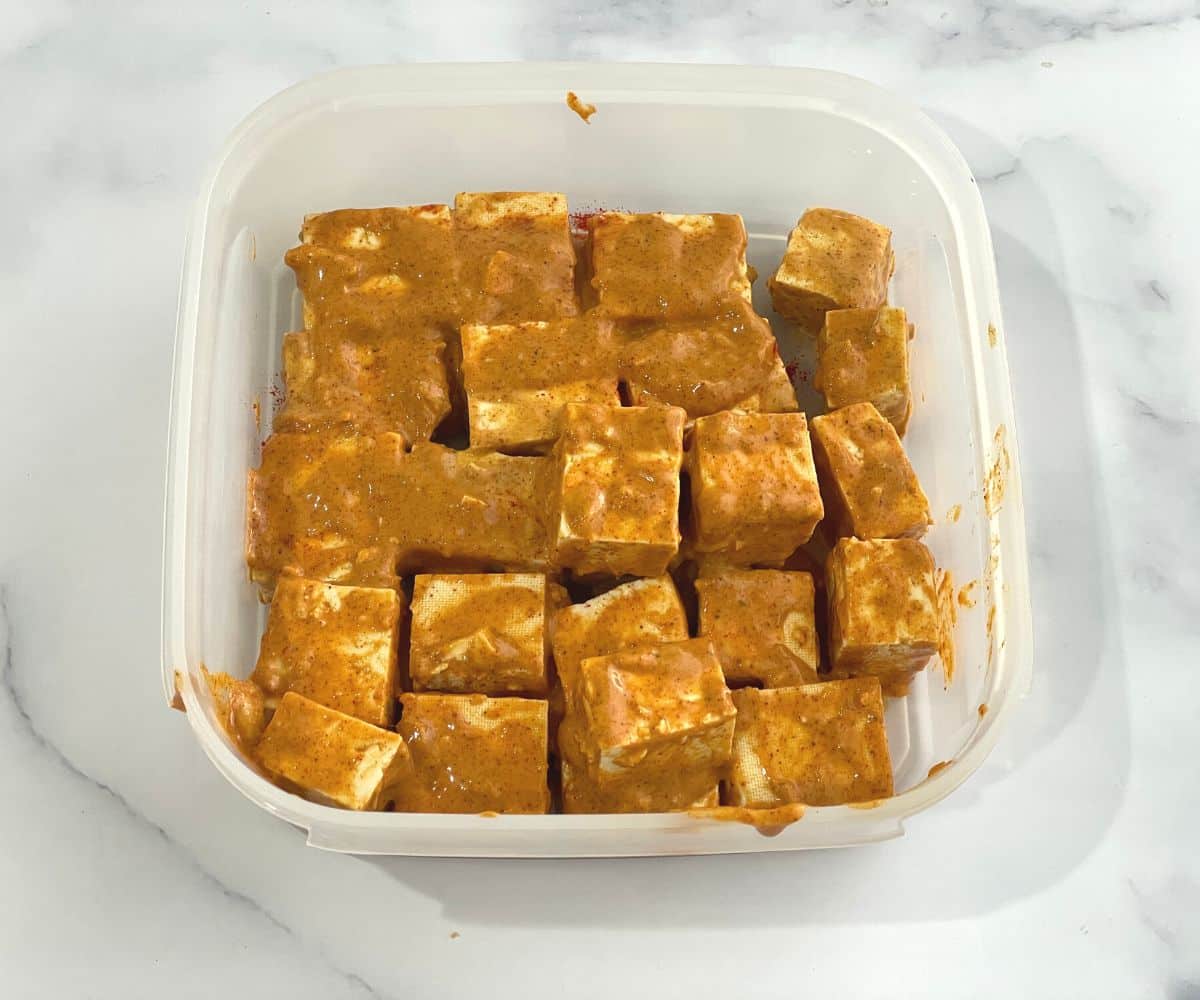 A container is with marinated tandoori tofu.