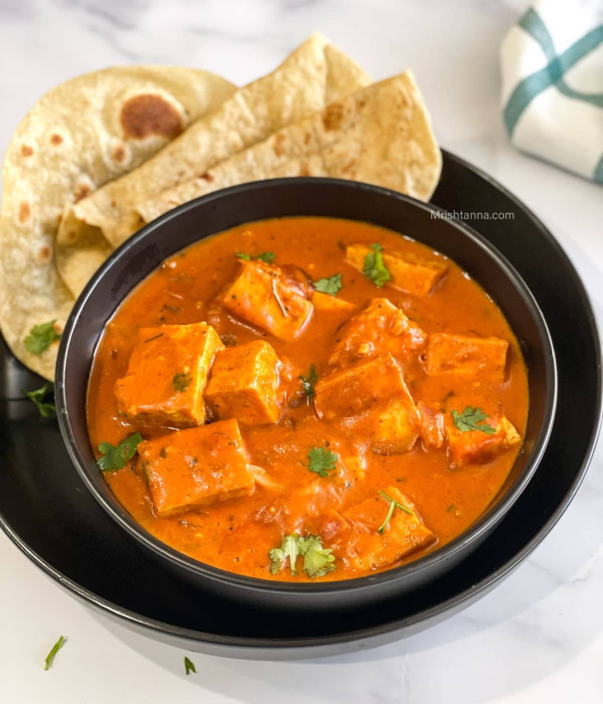 A bowl of tofu tikka masala is on the plate with roti's.