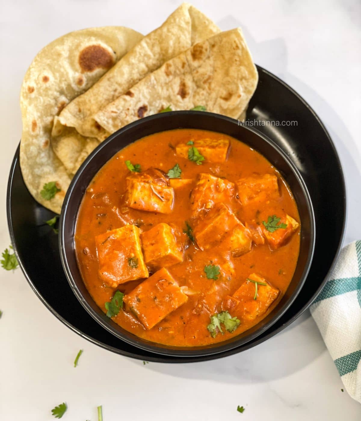 A bowl of vegan tikka masala curry is on the plate with chapati.