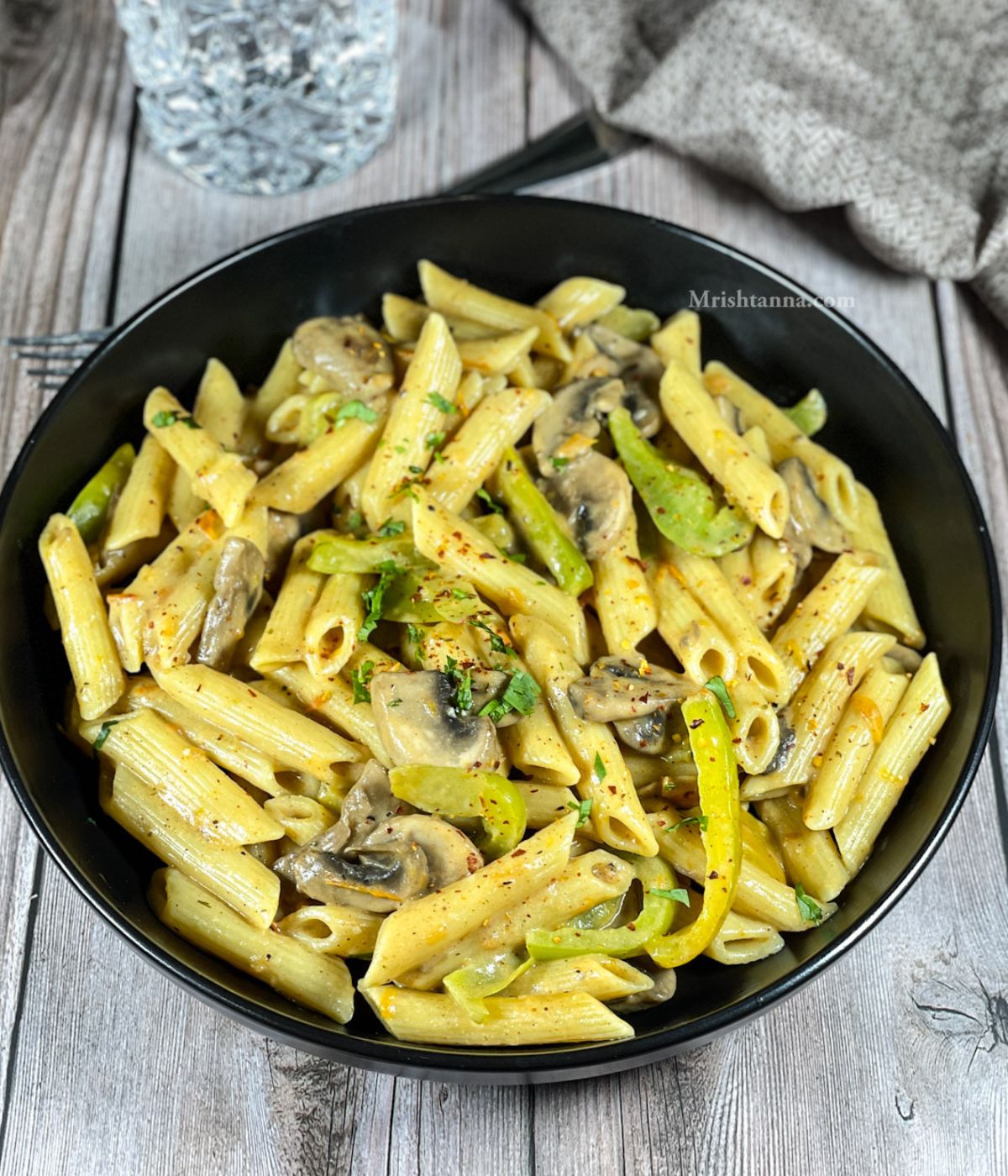 A plate of vegan cajun pasta is on the table with a glass of water.