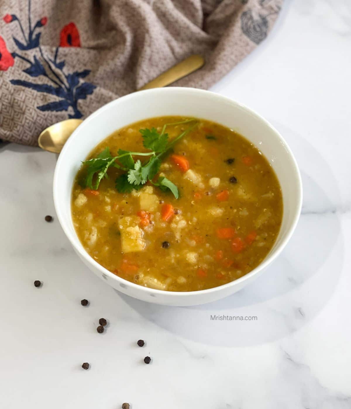 A bowl of vegan mulligatawny soup is on the white surface with a napkin and spoon on the side.