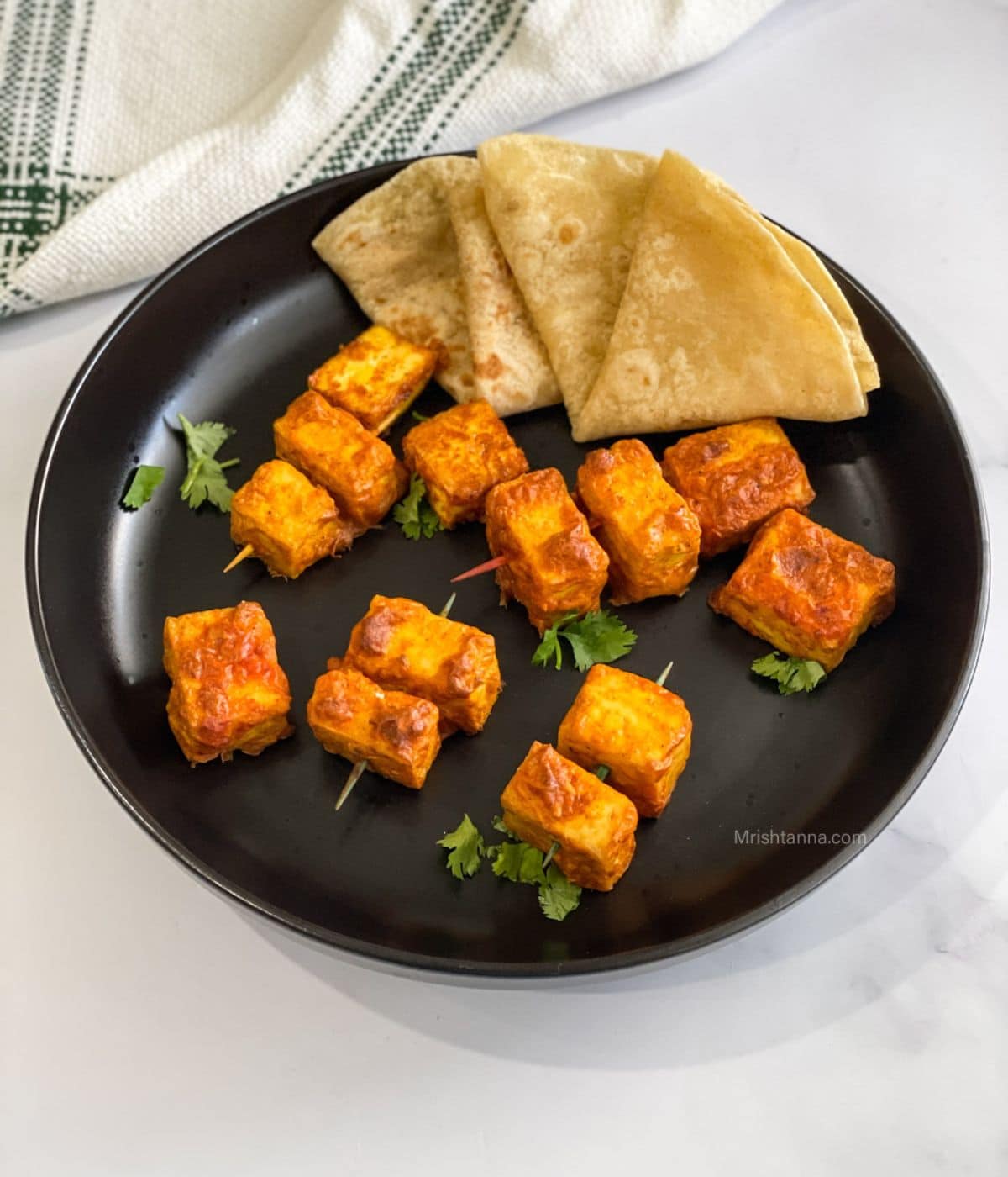 A plate of vegan tandoori tofu is on the table with chapati's.