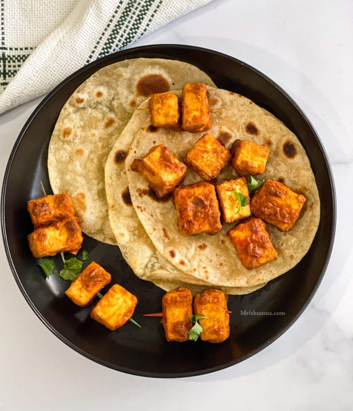 A plate of Tandoori tofu is on the chapati's.