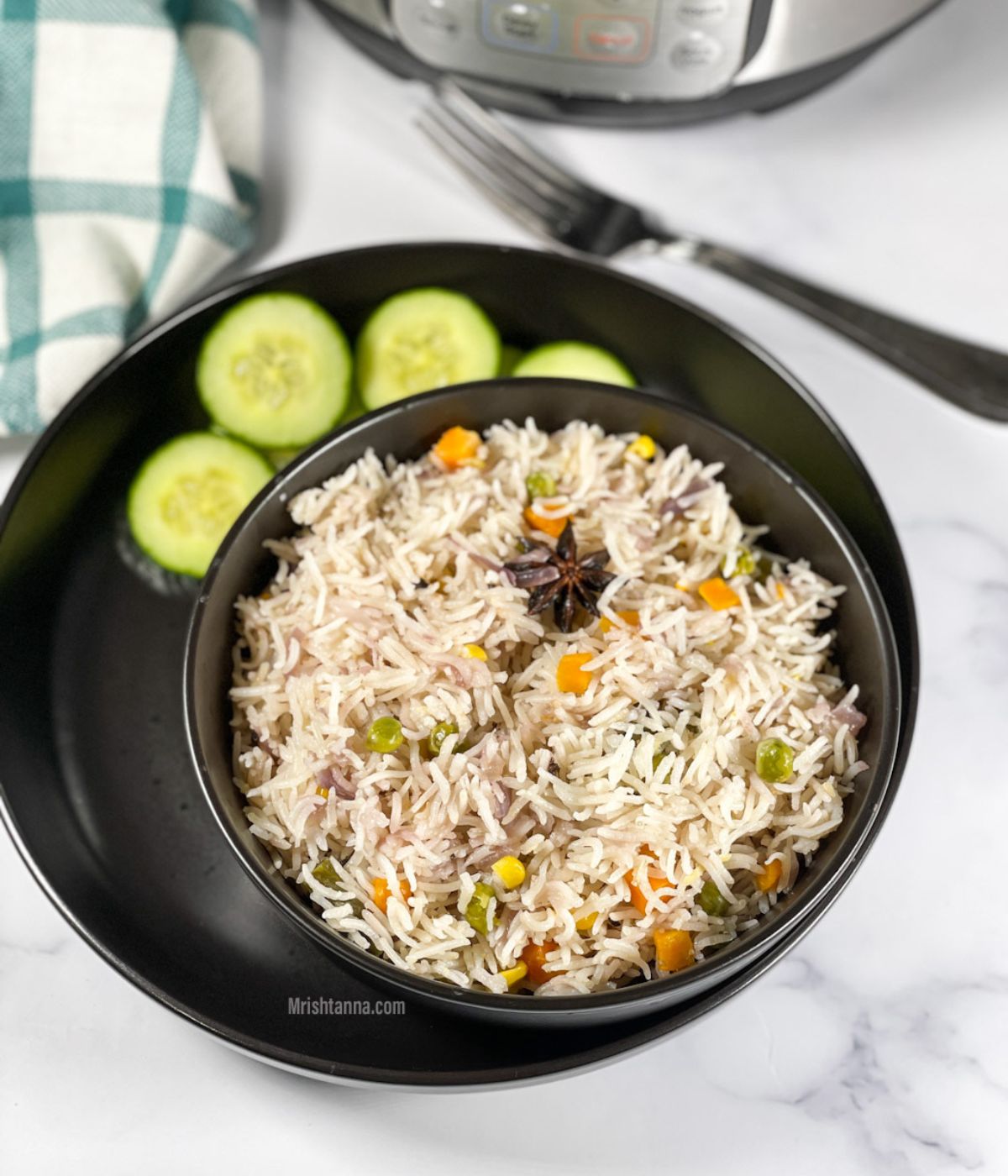 A bowl of vegetable pulao is on the table with cucumber slices.