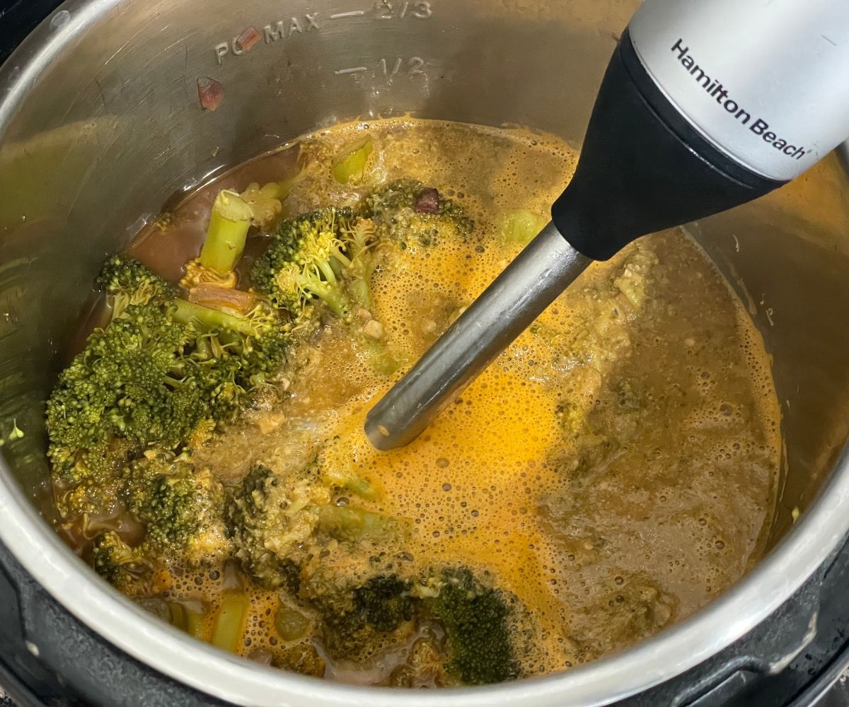 An instant pot is with broccoli soup and blending soup using a hand blender.