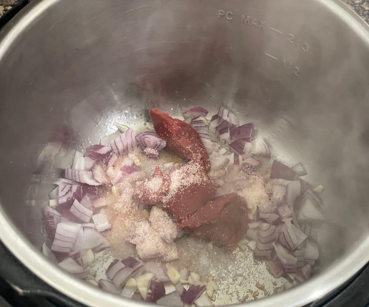An instant pot is with onions, tomato paste and chopped garlic on saute mode.