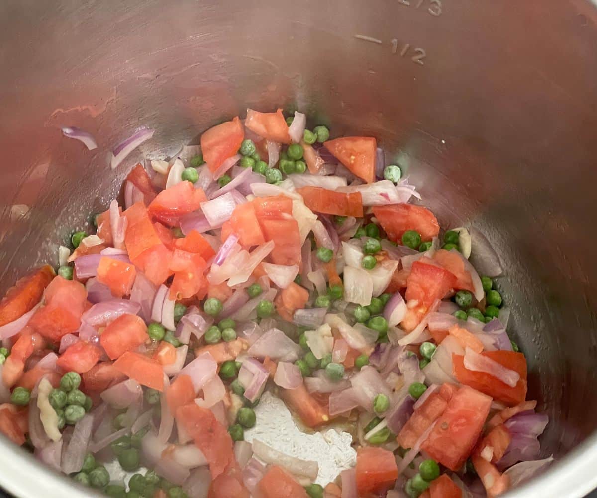 An instant pot is with tomatoes, peas on saute mode.