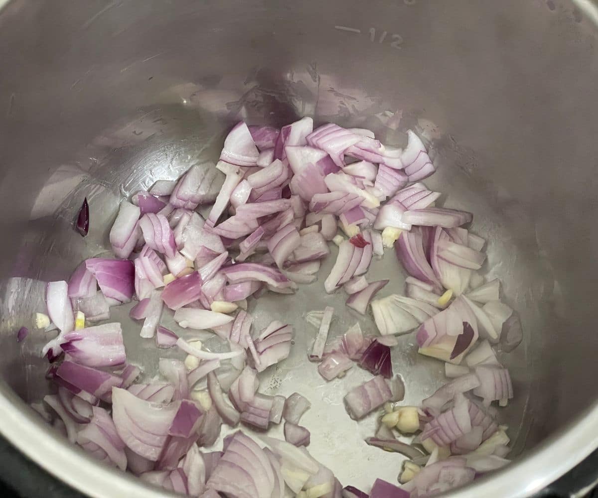 An instant pot is with oil and chopped onions.