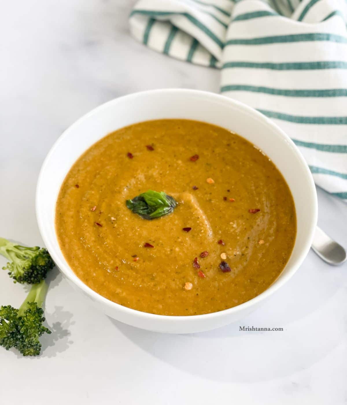 A bowl of broccoli tomato soup is on the table.