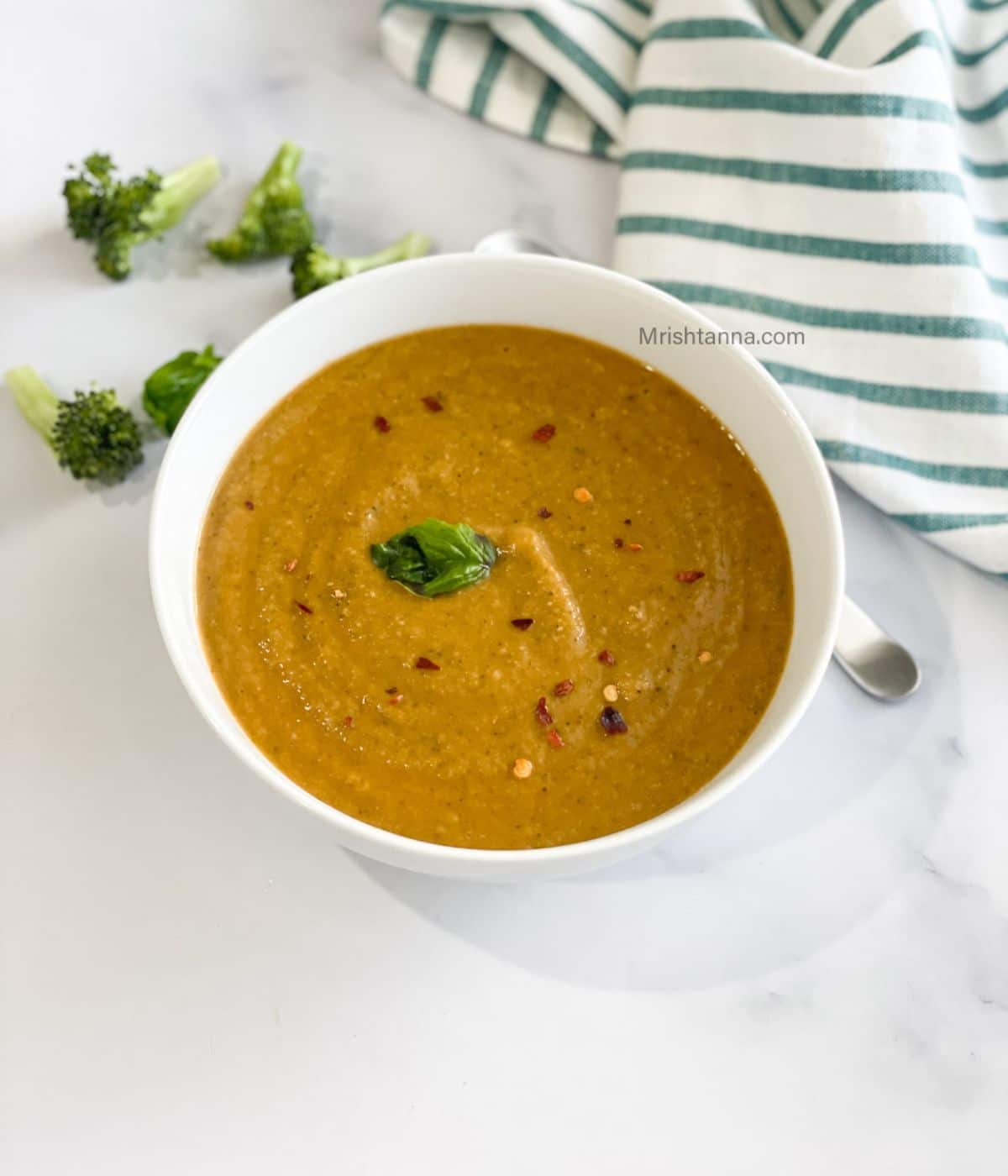 A white bowl is with vegan broccoli tomato soup.