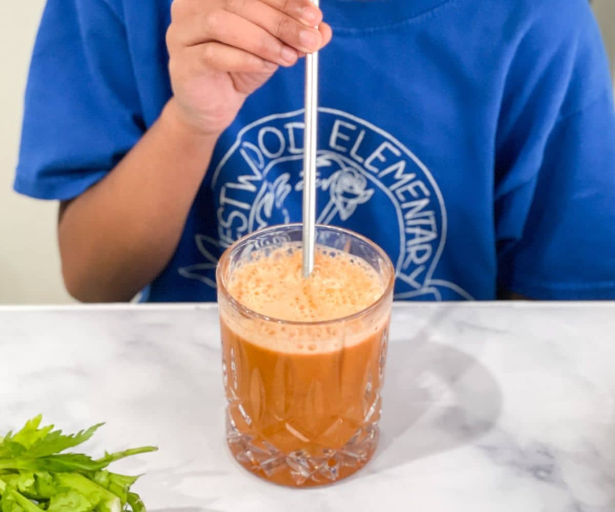 A girl is drinking a glass of carrot apple celery juice.