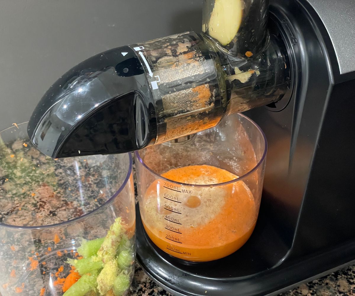 A juicer is juicing the fresh fruits and carrots.
