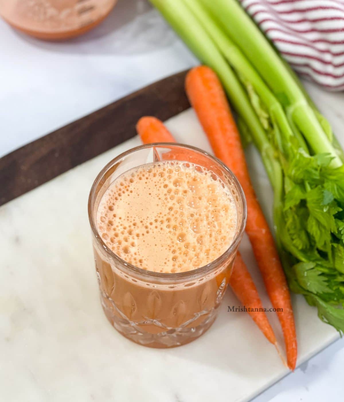 A galss of carrot celery apple juice is on the marble tray.