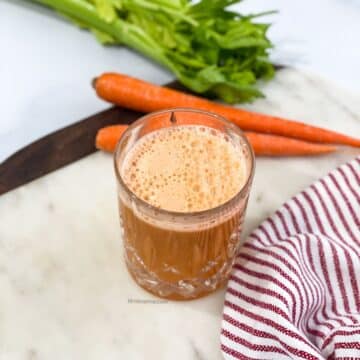 A glass of carrot celery juice is on the table.