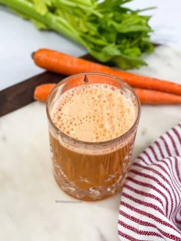 A glass of carrot celery juice is on the table.