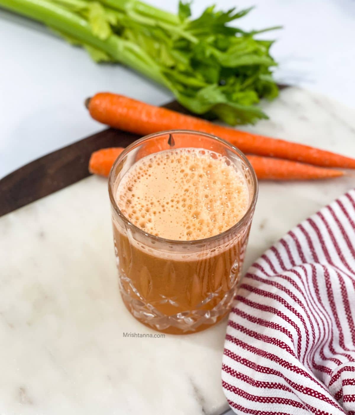 A glass of apple carrot celery juice is on the marble tray.