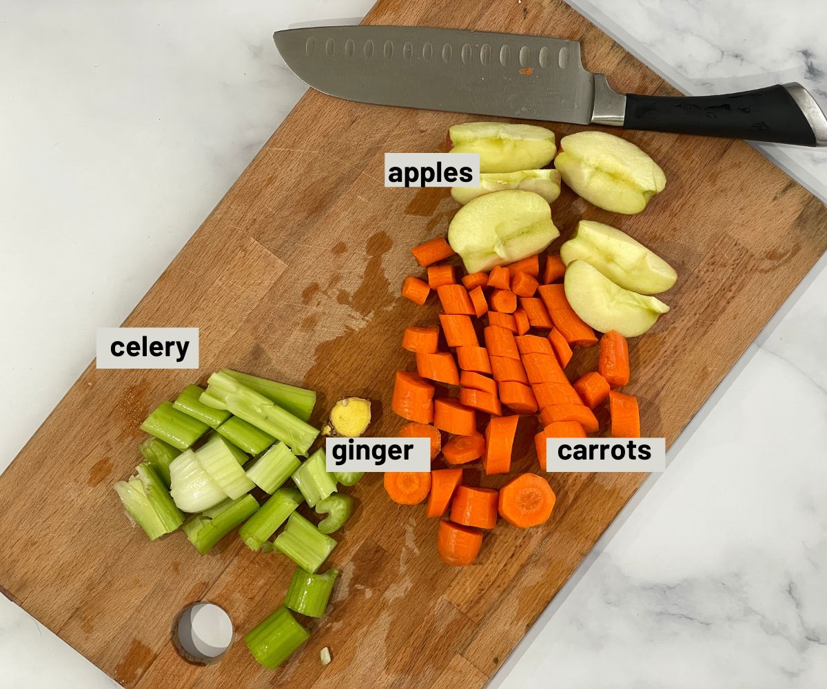 A wooden board is with chopped carrots, apple and celery for juice.