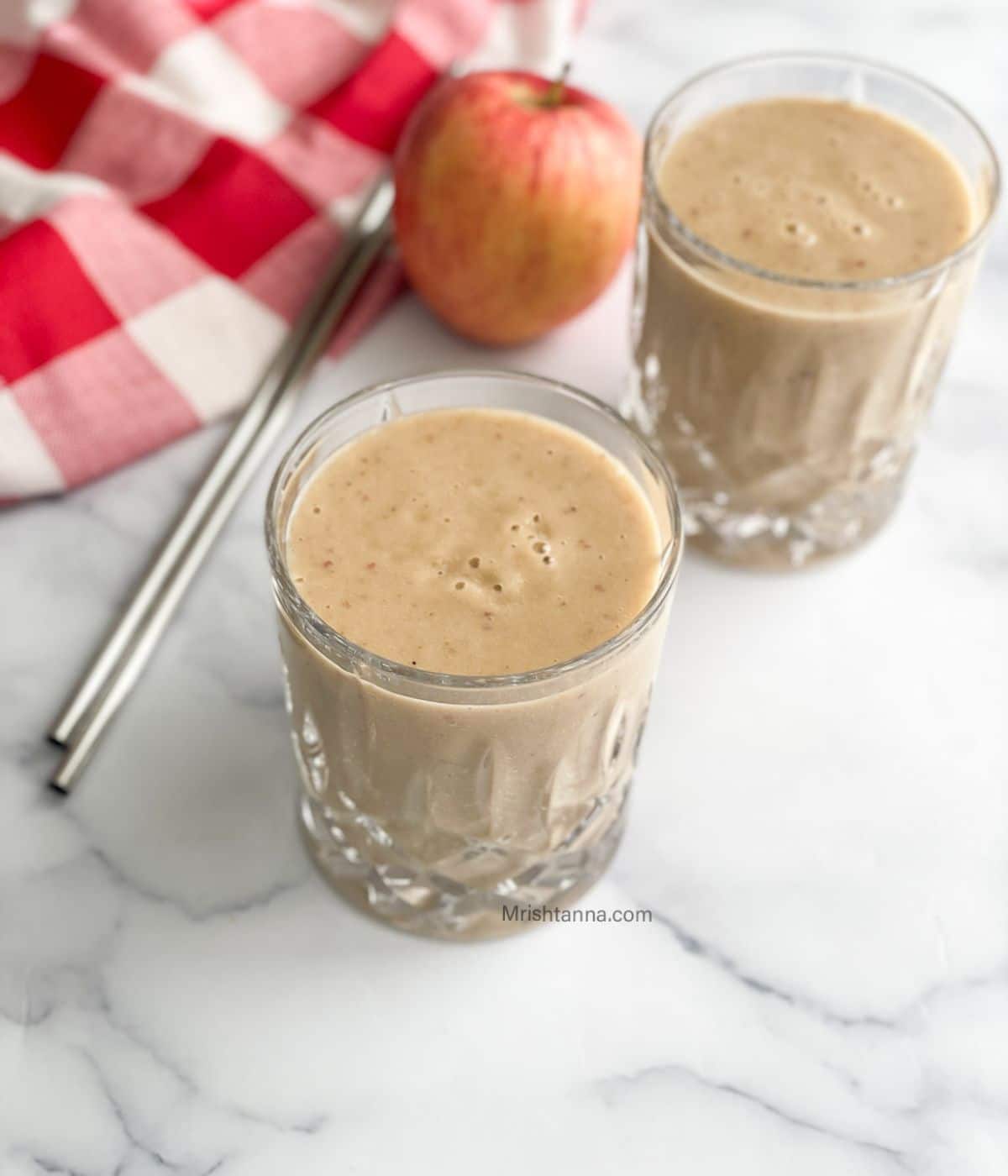 Two glasses are filled with banana apple smoothie.