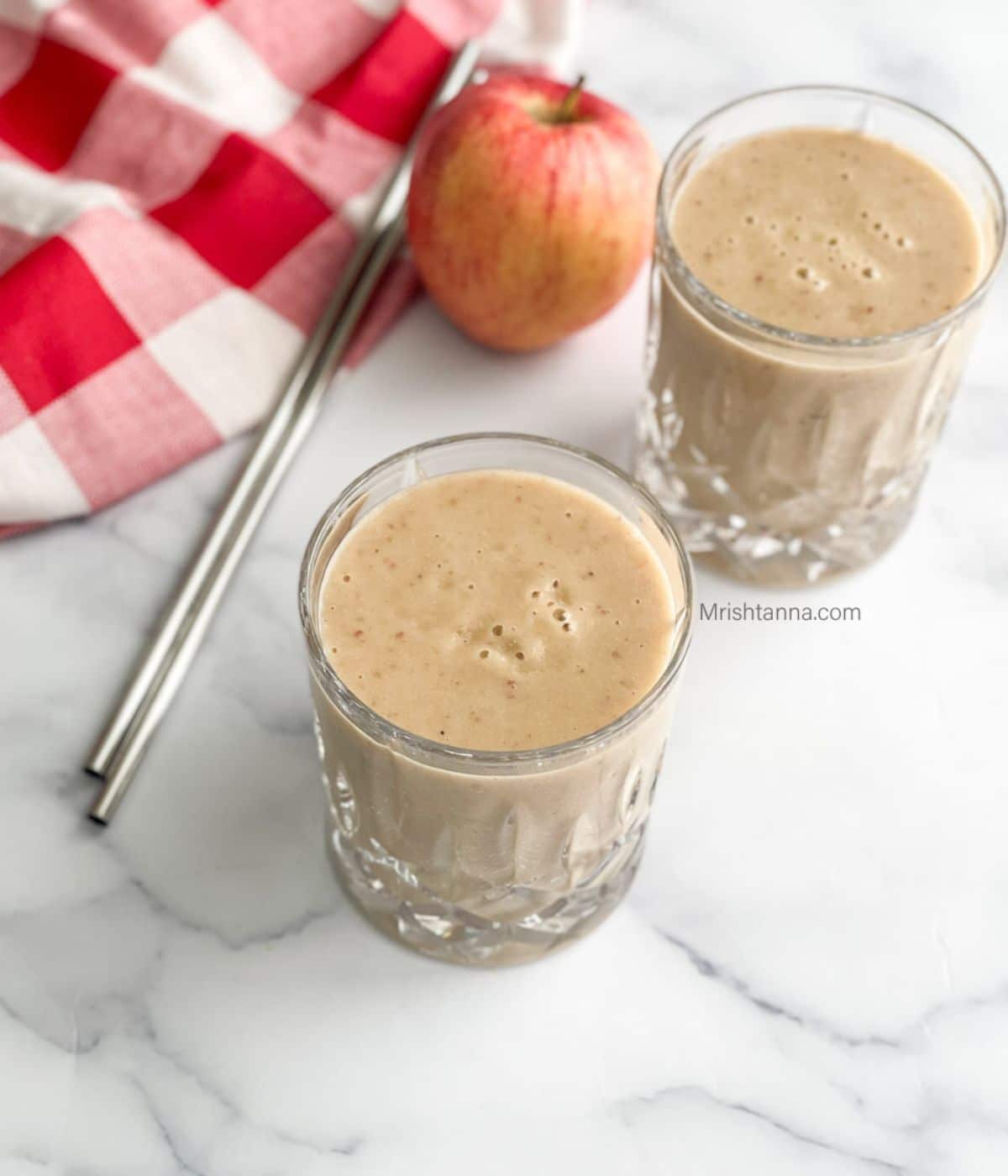 Two glasses of apple banana smoothies are on the table with two straws by the side.