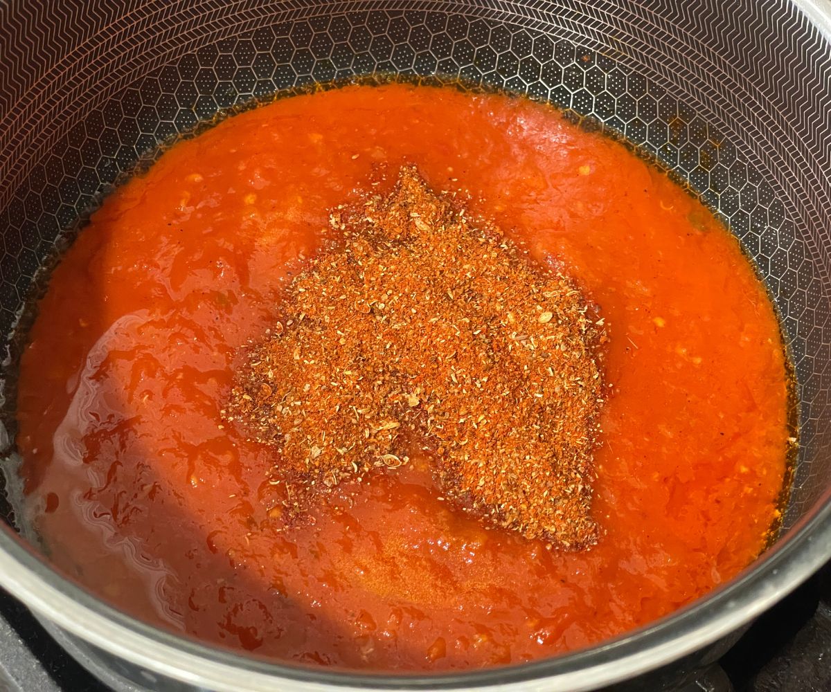 A pot is filled with tomato puree and spices over the heat.