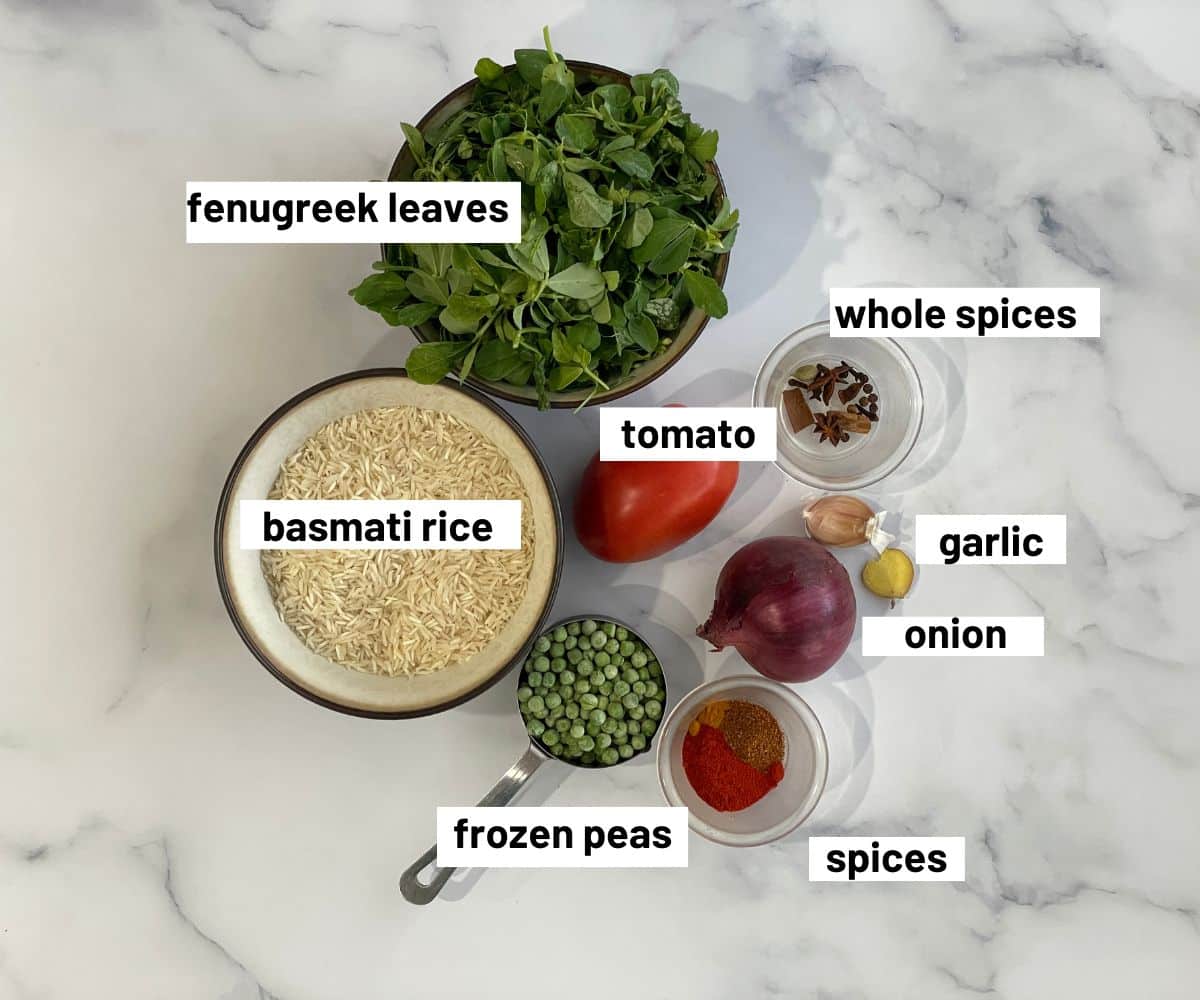 A table is filled with methi pulao ingredients.