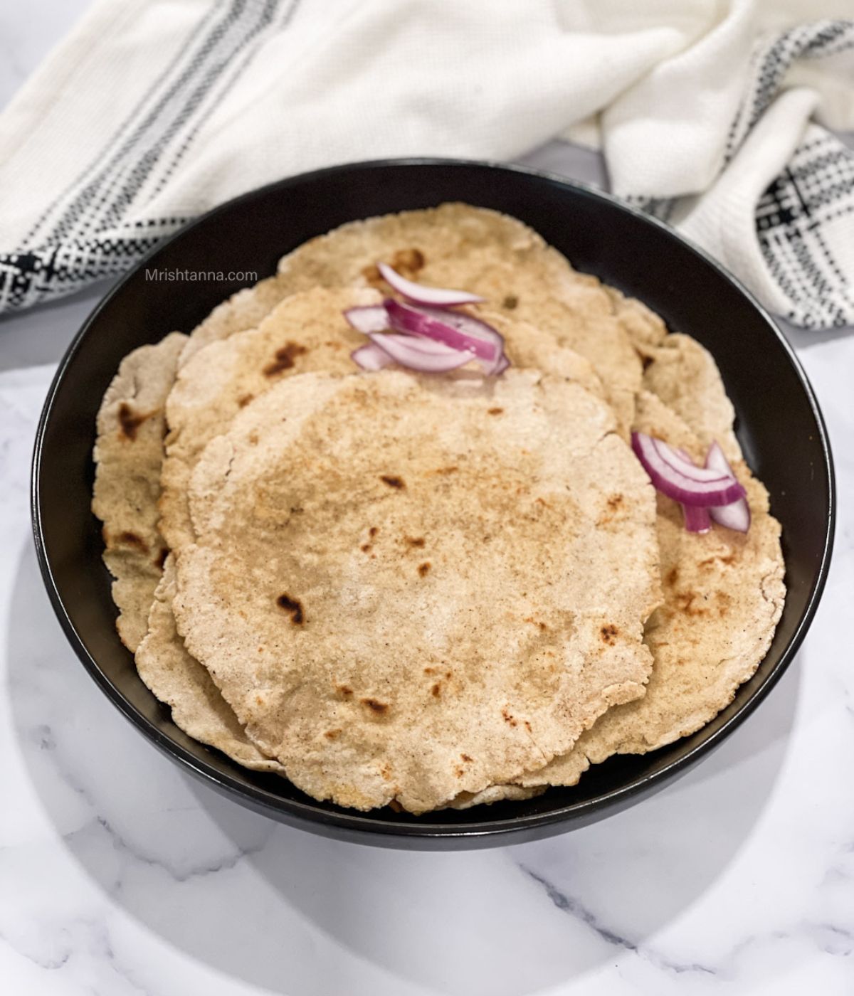 Staked sorghum rotis on the plate and topped with sliced onions.