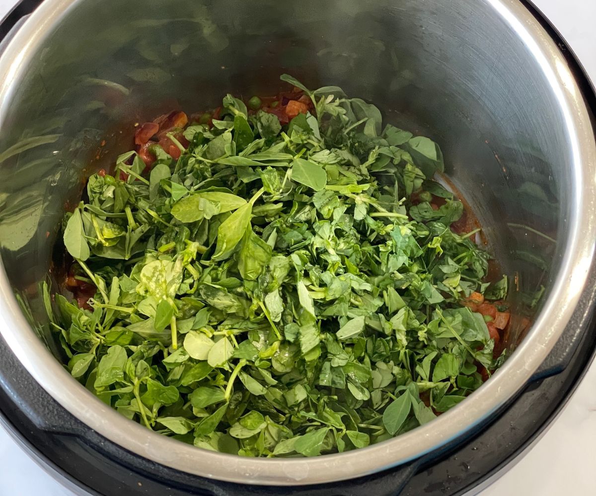 A pot is with spices and fresh fenugreek leaves on saute mode.