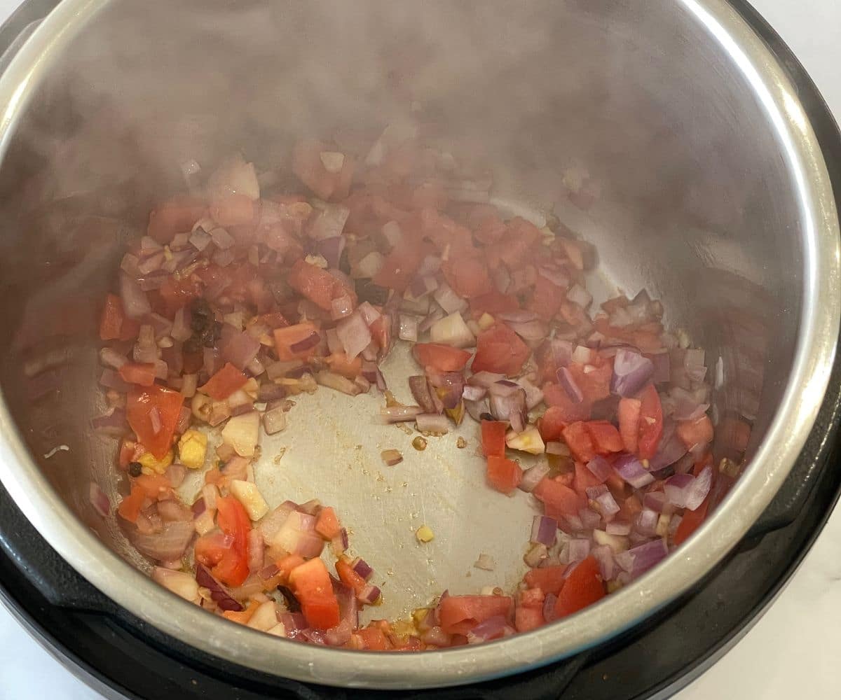 An instant pot is with spices and onions on saute mode.