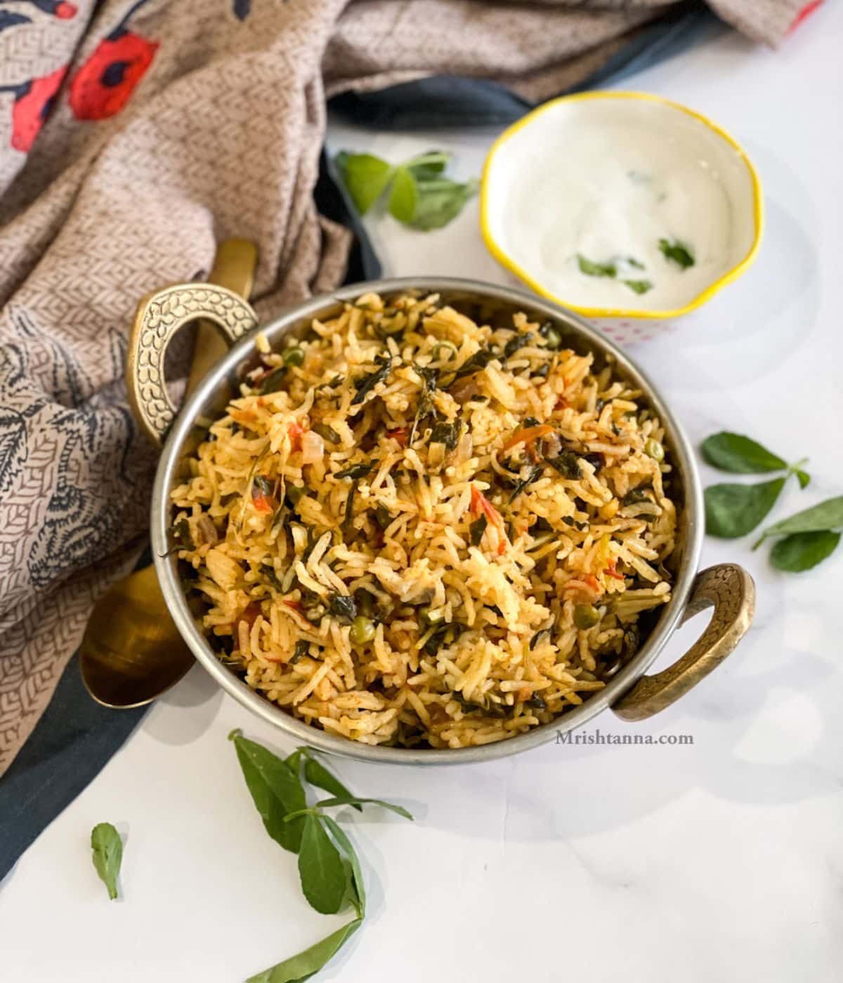 A bowl of methi rice is on the table along with bowl of raita.