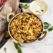 A copper bowl is filled with methi pulao on the table with napkins.