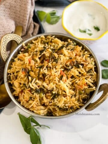 A copper bowl is filled with methi pulao on the table with napkins.