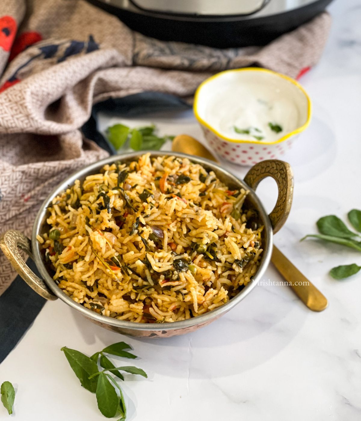 A bowl of fenugreek leaves rice and raita is on the table along with a spoon.