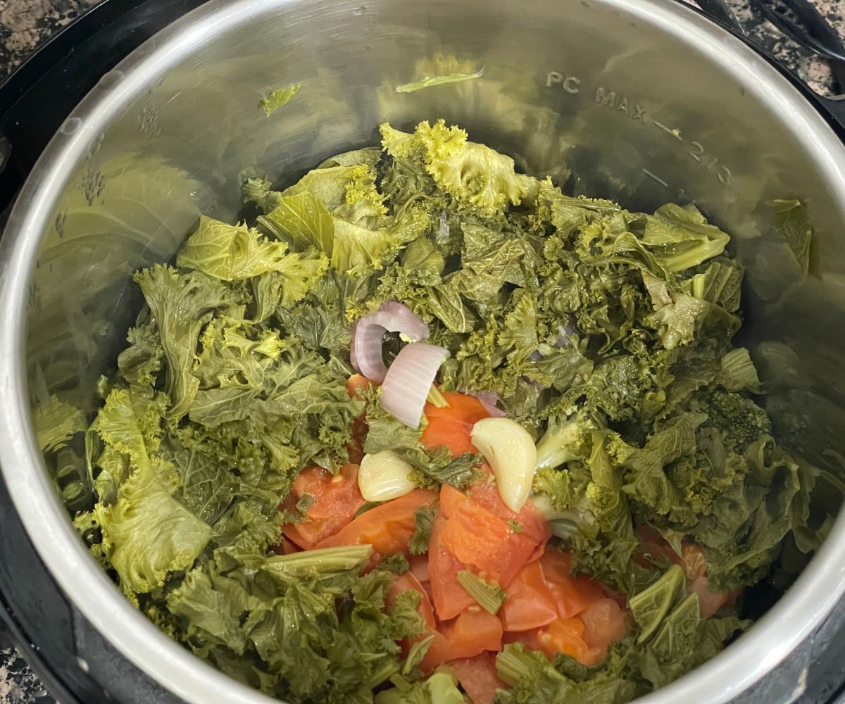 An instant pot is with cooked veggies and greens for sarson ka saag.