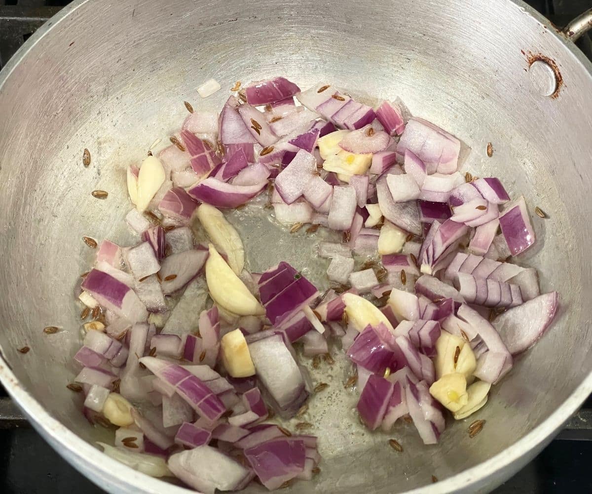 A pan is with chopped onions and garlic for saag.