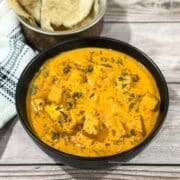 A bowl of tofu makhani curry is on the table with rotis by the side.