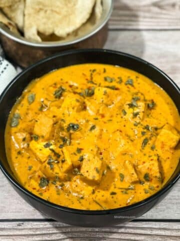 A bowl of tofu makhani curry is on the table with rotis by the side.