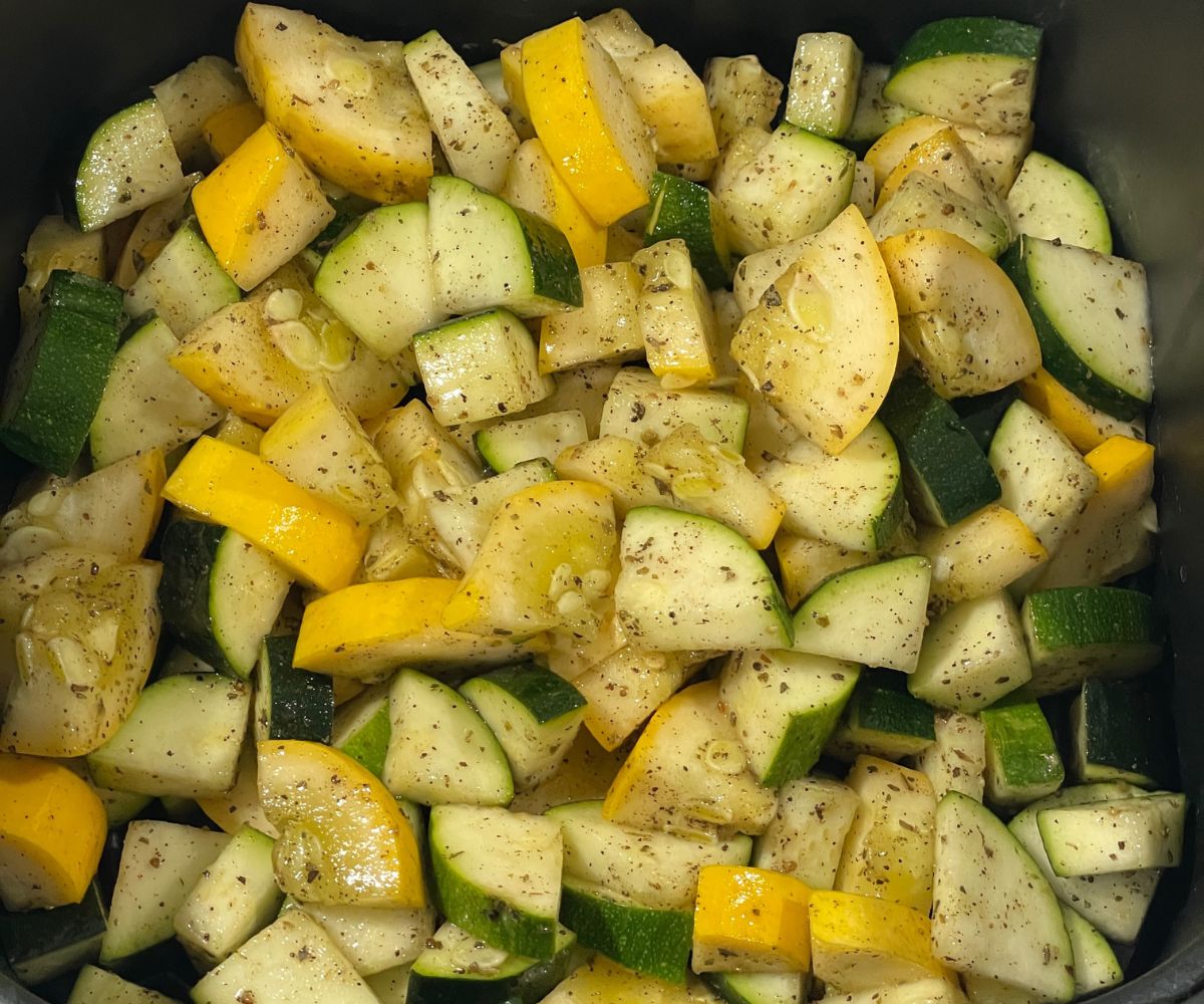 The air fryer basket is seasoned with zucchini and squash.