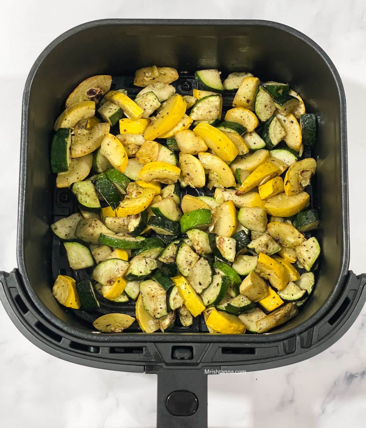 Air fryer basket is with zucchini and squash.