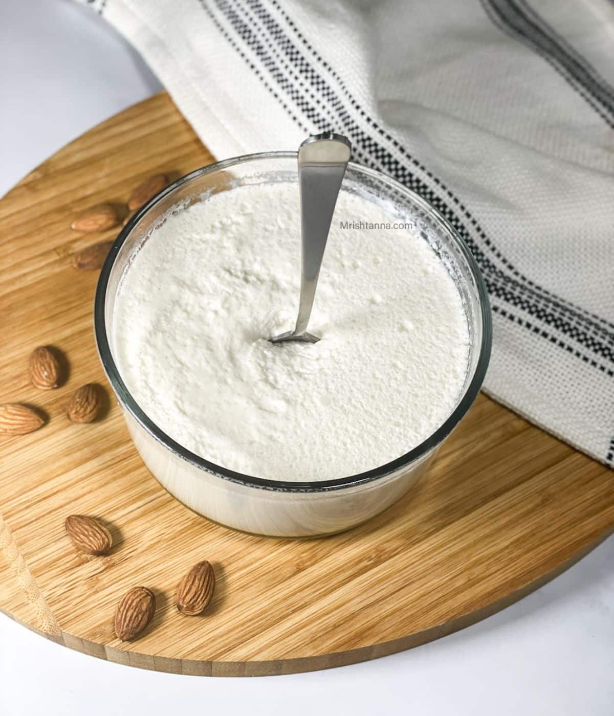 A glass bowl is with almond milk yogurt and a spoon is inserted.