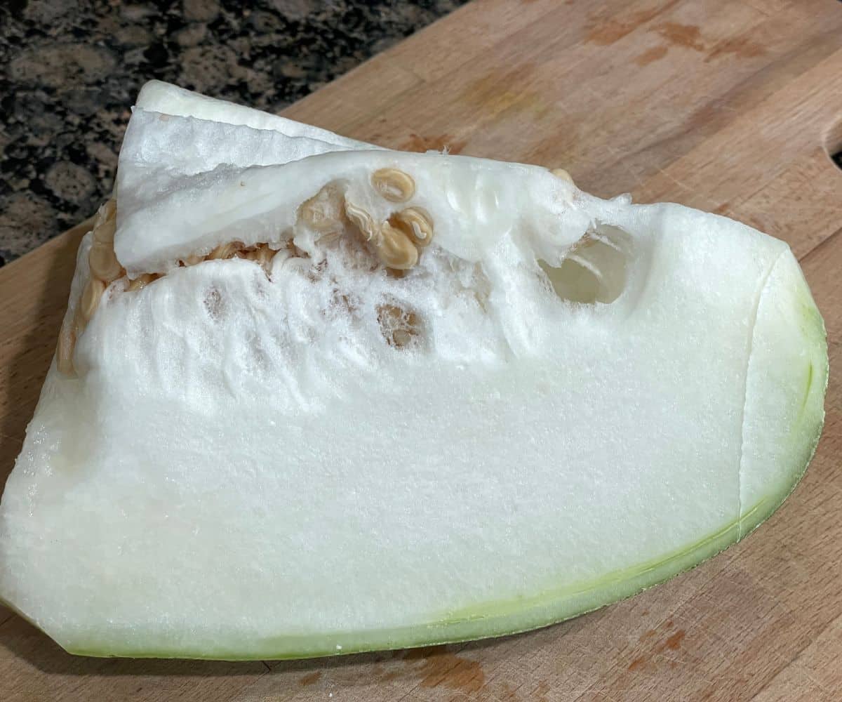 A cutting board is with a quarter of white pumpkin.