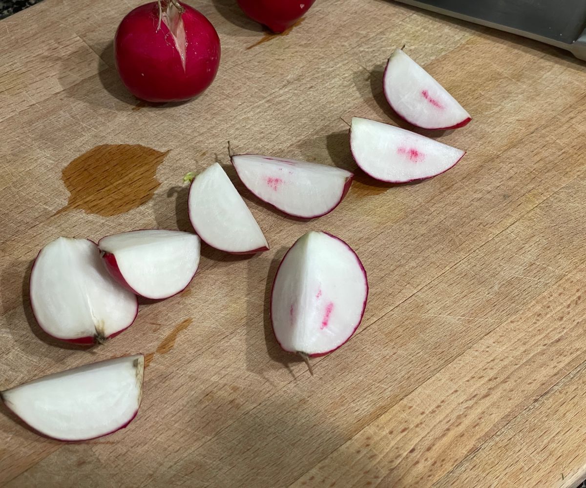 A wooden cutting board is with sliced radishes.
