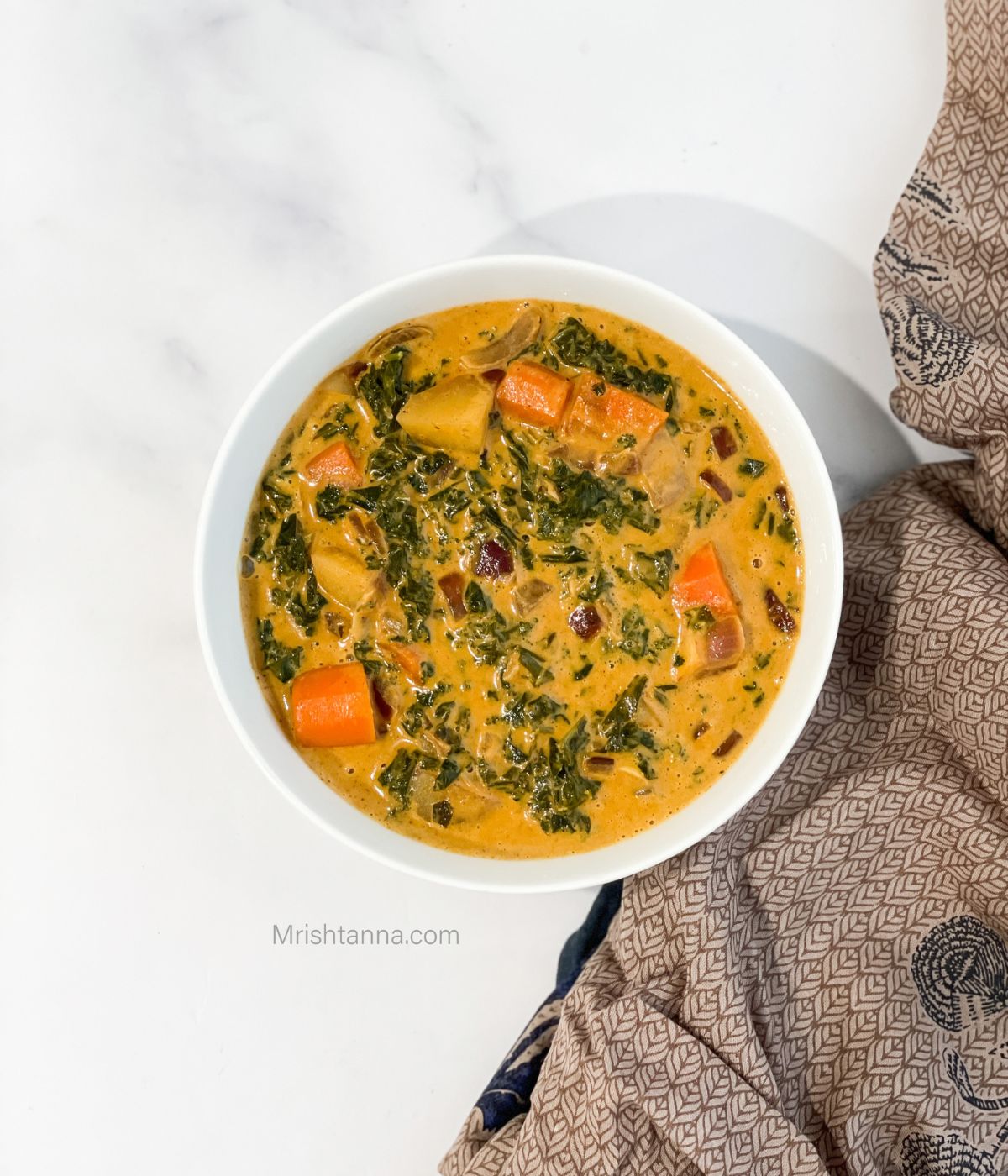 A bowl of kale curry with veggies on the white surface.