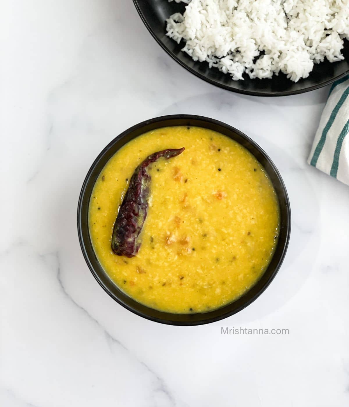 A bowl is with Bengali Moong dal and topped with red chli.